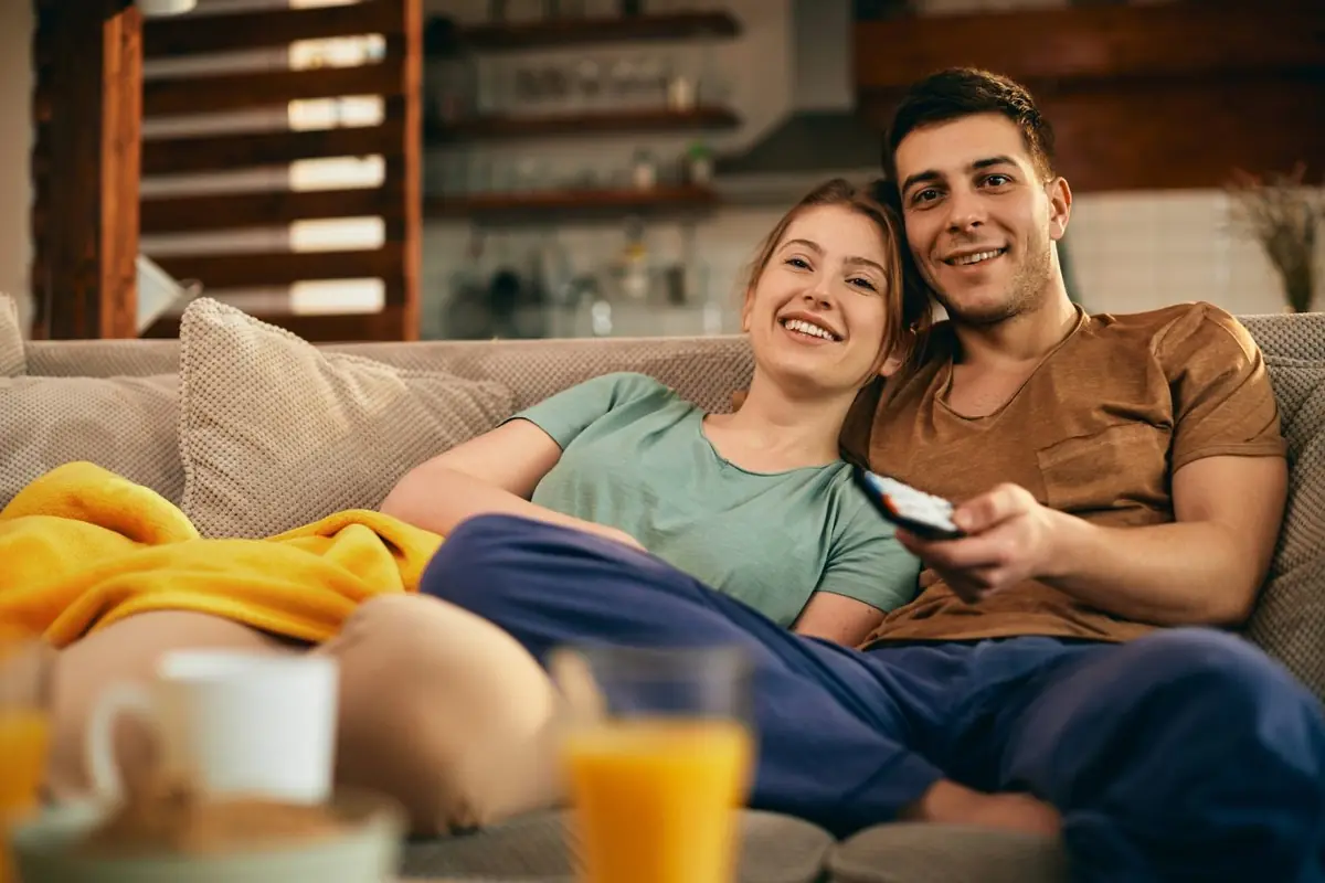 Paar entspannt mit Fernbedienung auf dem Sofa nach dem Kauf des IPTV Jahresabos